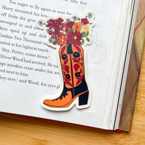 Könnte beinhalten: Ein Aufkleber mit einem Cowboy-Stiefel, in dem ein Strauß Herbstblumen steckt. Der Stiefel ist orange und schwarz mit einem Blumenmuster. Die Blumen sind rot, orange, gelb und weiß.