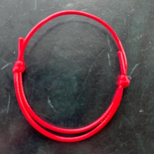 May include: A bright red braided bracelet made of a thick cord.