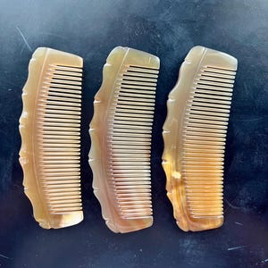 May include: Three hair combs made of translucent, light brown material with a smooth, polished finish. Each comb features a curved, scalloped outer edge and a series of fine, parallel teeth designed for grooming hair with precision and ease.