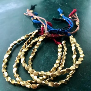 Peut inclure: Quatre bracelets en perles dorées avec des liens en ficelle de couleurs. Les bracelets sont faits de petites perles de forme ovale.