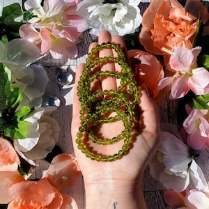 May include: A stack of green gemstone bracelets, each with a different number of beads, are held in a person's hand. The bracelets are made of small, round beads.