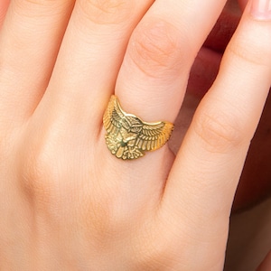 Peut inclure: Une bague en or avec un motif d'aigle détaillé. La bague est portée sur un doigt avec un vernis à ongles rose clair.