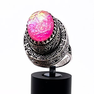May include: A silver ring with an ornate design and a pink oval-shaped gemstone.