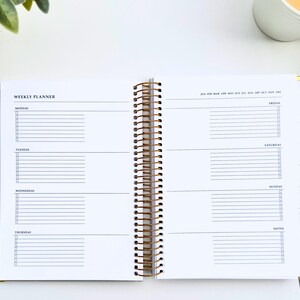 May include: Open weekly planner with a gold spiral binding. The planner is open to a spread with lined sections for each day of the week, with checkboxes. The top of the page reads "WEEKLY PLANNER".