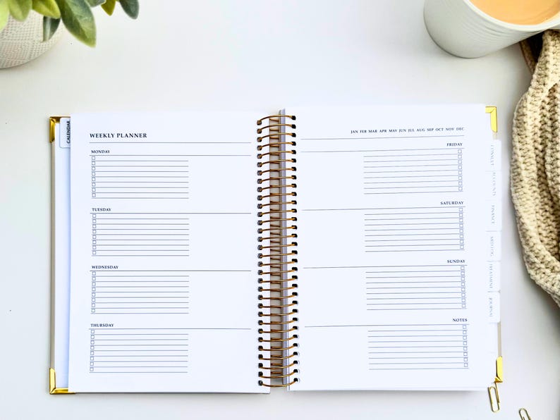 May include: Open weekly planner with a gold spiral binding. The planner is open to a spread with lined sections for each day of the week, with checkboxes. The top of the page reads "WEEKLY PLANNER".