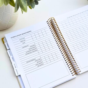 May include: Open planner with gold spiral binding and tabs labeled "Consult", "Accounts", "Finance", "Med Log", and "Treatment". The open pages display a "Stimulation Monitoring" chart with sections for cycle day, lab results, and follicle results.