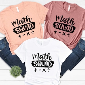 May include: Three t-shirts in peach, mauve, and white, each with the words "Math SQUAD" in a black, bold font. Below the text are math symbols: plus, minus, multiplication, and division. The shirts are paired with blue jeans.