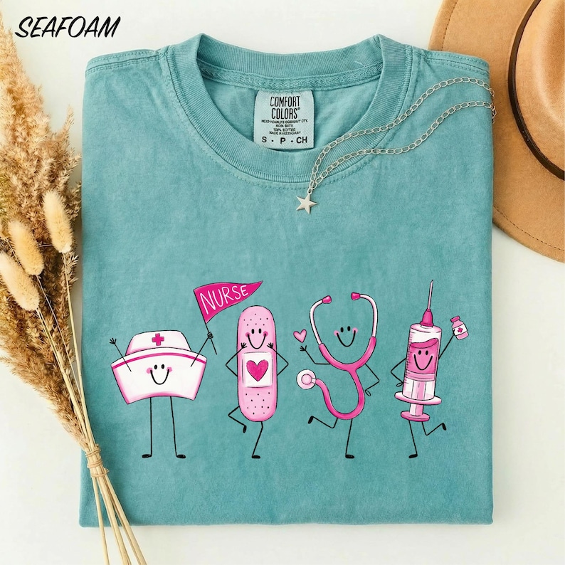 A turquoise t-shirt with a graphic design depicting four cartoon nurse characters, including a nurse's hat, stethoscope, bandage, and syringe, along with the text "NURSE" and "CONFIDENCE COLOR".