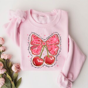 a pink sweater with a bow and cherries on it