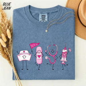 A blue t-shirt with a graphic design depicting four cartoon nurse characters, including a nurse's hat, bandages, a stethoscope, and a syringe, along with the text "NURSE" and a star.