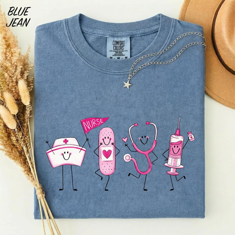 A blue t-shirt with a graphic design depicting four cartoon nurse characters, including a nurse's hat, bandages, a stethoscope, and a syringe, along with the text "NURSE" and a star.