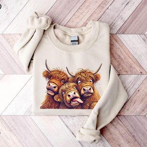 A beige sweater with a printed image of three yaks with horns and wide-open mouths, appearing to be making a funny or playful expression.