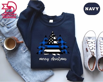 May include: Navy blue sweatshirt with a Christmas tree design incorporating a blue line, American flag, and blue plaid pattern. The words "merry christmas" are printed in white. The sweatshirt has long sleeves and a crew neck.