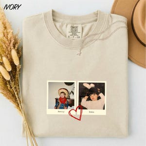 a beige t-shirt with a printed photo of two children, one wearing a cowboy hat and the other wearing a white shirt, along with a red heart symbol.