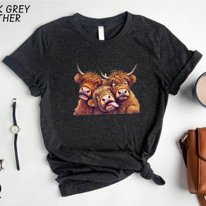 a black t-shirt with a graphic of three yaks or long-haired cows, along with a watch, a cup of coffee, and a handbag.