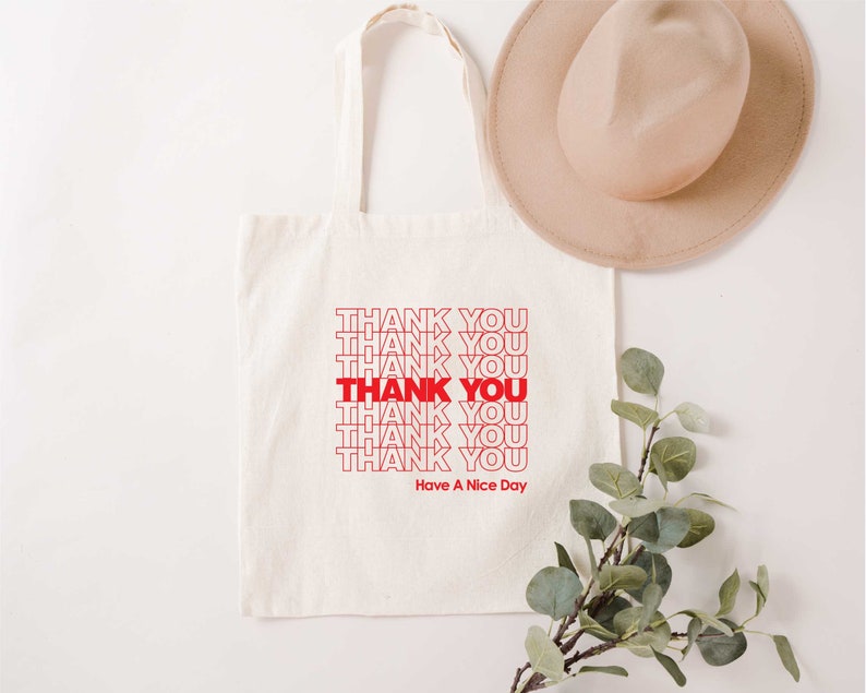 May include: A white canvas tote bag with red text that says "THANK YOU" repeated multiple times. The text is in a retro style font. The bag also has the text "Have A Nice Day" printed on it.
