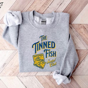 a grey sweatshirt with the words the tinyned fish on it