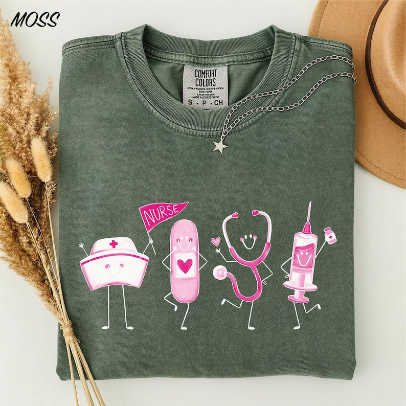a green t-shirt with a graphic design of four cartoon-style medical professionals, including a nurse, a stethoscope, a syringe, and a pill bottle, all depicted in a playful and colorful manner.