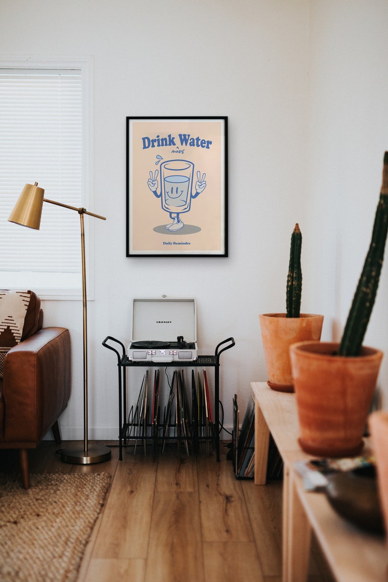 K&ouml;nnte beinhalten: Ein schwarzer gerahmter Poster mit einer Cartoon-Illustration eines Glases Wasser mit Armen und Beinen. Das Glas l&auml;chelt und zeigt mit beiden H&auml;nden das Peace-Zeichen. Der Text auf dem Poster lautet "Drink Water A Daily Reminder".
