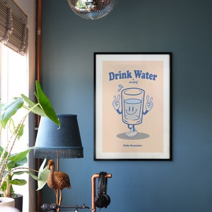 K&ouml;nnte beinhalten: Ein gerahmtes Poster mit einer Cartoon-Illustration eines Glases Wasser mit Armen und Beinen. Das Glas l&auml;chelt und zeigt mit beiden H&auml;nden das Peace-Zeichen. Der Text auf dem Poster lautet "Drink Water More Daily Reminder".