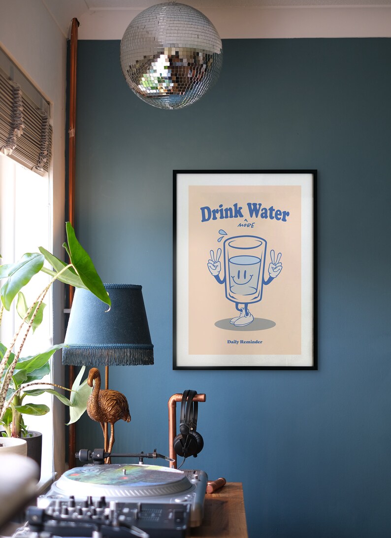 K&ouml;nnte beinhalten: Ein gerahmtes Poster mit einer Cartoon-Illustration eines Glases Wasser mit Armen und Beinen. Das Glas l&auml;chelt und zeigt mit beiden H&auml;nden das Peace-Zeichen. Der Text auf dem Poster lautet "Drink Water More Daily Reminder".