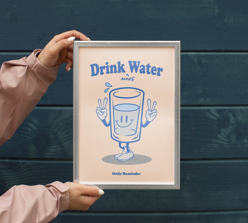 K&ouml;nnte beinhalten: Ein gerahmtes Poster mit einem hellrosa Hintergrund und einer Cartoon-Illustration eines Glases Wasser mit einem l&auml;chelnden Gesicht. Der Text auf dem Poster lautet "Drink Water More Daily Reminder".