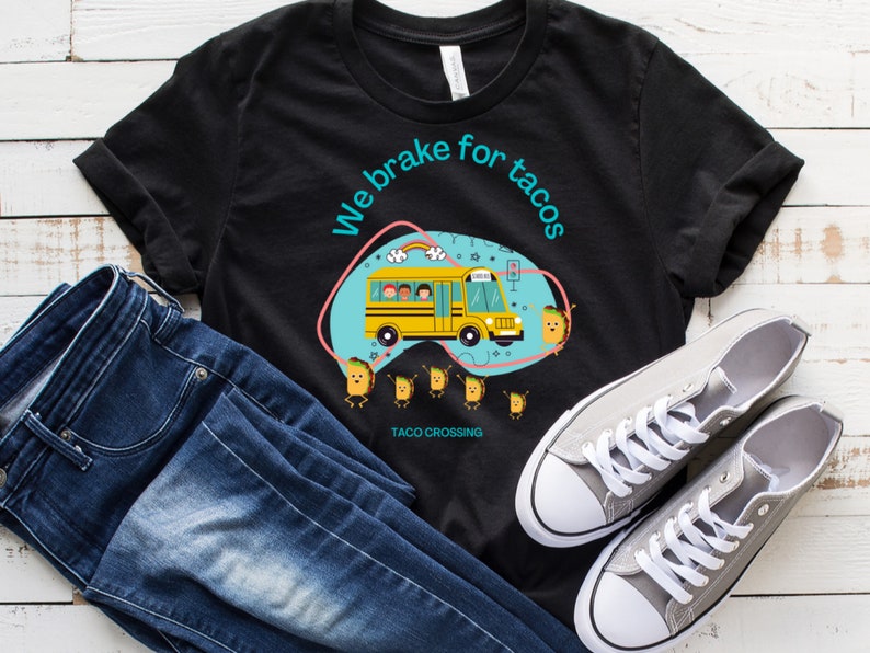May include: Black t-shirt with a graphic of a school bus with the text "We brake for tacos" and a group of tacos crossing the street. The text "Taco Crossing" is below the graphic.