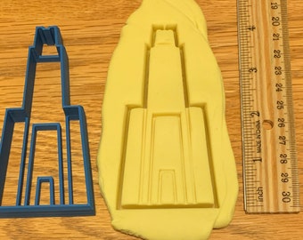 Könnte beinhalten: Ein blauer Plastik-Ausstecher in Form eines hohen Gebäudes mit einem spitzen Dach, neben einem gelben Abdruck des Ausstechers in einem Teigblock. Ein Lineal ist rechts im Bild zu sehen.