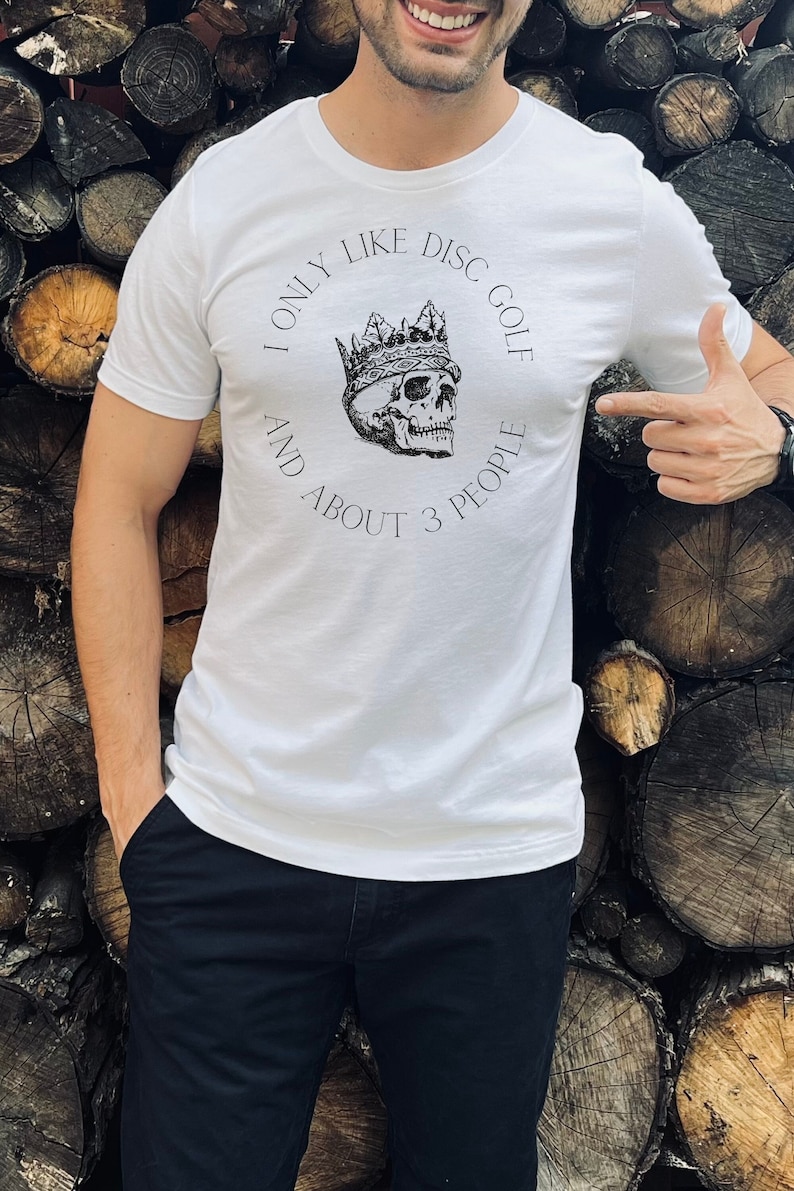 Peut inclure: T-shirt blanc avec un graphique noir et blanc d'un cr&acirc;ne portant une couronne. Le texte sur le t-shirt est "I only like disc golf and about 3 people."
