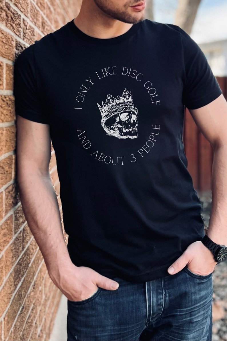Peut inclure: Un t-shirt noir avec un motif blanc d'un cr&acirc;ne portant une couronne. Le texte sur le t-shirt est "I only like disc golf and about 3 people."