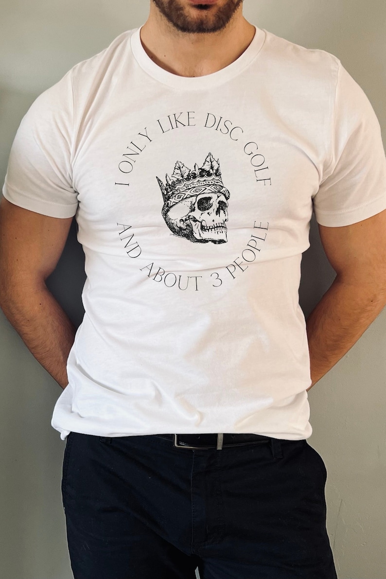 Peut inclure: T-shirt blanc avec un graphique noir et blanc d'un cr&acirc;ne portant une couronne. Le texte sur le t-shirt est "I only like disc golf and about 3 people."