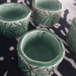 Puede incluir: Cuatro pequeños cuencos de cerámica verde con un esmalte blanco y un patrón de estrella. Los cuencos están dispuestos en un patrón escalonado sobre una tela negra y blanca.