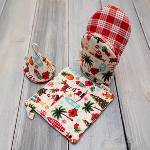 Puede incluir: Un juego de tres textiles de cocina con un tema navideño tropical. Incluye un guante de horno a cuadros rojos y blancos, un salvamanteles cuadrado y un salvamanteles en forma de lágrima. Todos los artículos tienen un fondo crema con palmeras, Papá Noel surfeando y renos.