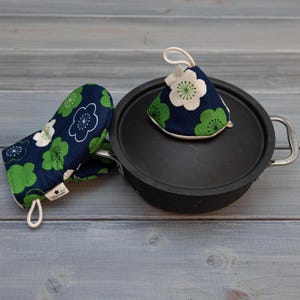 May include: A set of two blue and green floral pot holders. One is a mitten style and the other is a cone shape. Both have white flowers with green centers.