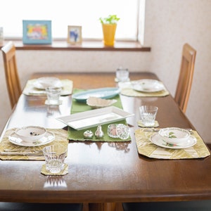 Puede incluir: Un juego de comedor de madera con cuatro sillas, cubiertos y manteles individuales verdes. La mesa est&aacute; puesta con platos blancos, cuencos, vasos y cubiertos. Tambi&eacute;n hay dos peque&ntilde;os saleros y pimenteros de plata en la mesa.