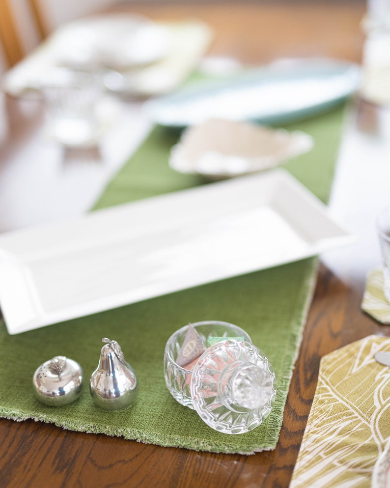 Puede incluir: Un plato rectangular blanco, dos saleros y pimenteros de plata en forma de pera y un frasco de vidrio con tapa lleno de caramelos de colores sobre un mantel verde.