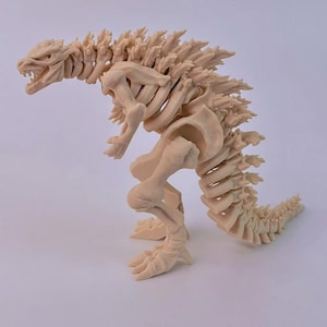 May include: A beige, articulated Godzilla skeleton model. The model is posed in a dynamic stance, showcasing the intricate skeletal structure. The spines along the back and tail are clearly defined, and the mouth is open, revealing teeth.