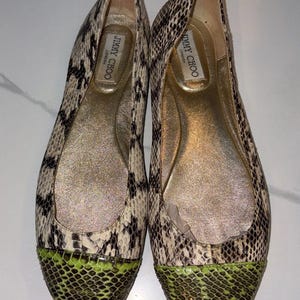 Puede incluir: Un par de bailarinas Jimmy Choo London con estampado de piel de serpiente en tonos beige, negro y blanco. Las punteras redondeadas están acentuadas con una textura de piel de serpiente en color verde lima. Las plantillas son doradas con el logo.