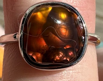 Puede incluir: Un anillo de plata con una piedra de ágata grande de forma ovalada. La piedra es una mezcla de colores marrón, naranja y rojo con un patrón de remolino.
