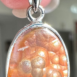 May include: A silver pendant necklace with a large oval-shaped agate stone. The stone is a light pink color with brown and white swirls and a iridescent sheen.