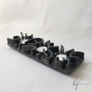 May include: A black ceramic candle holder with a geometric design. The holder has spaces for four white candles and features curved and angular shapes. The base is rectangular, and the overall aesthetic is modern and minimalist.