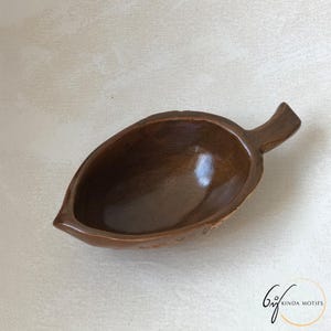 May include: A leaf-shaped wooden bowl with a dark brown finish. The bowl has a small handle and a smooth, polished interior. The bowl is designed for serving or display, and is likely handmade.
