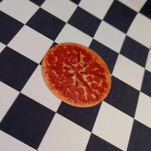 May include: A pepperoni pizza with a brown crust and red pepperoni slices on a black and white checkered background.