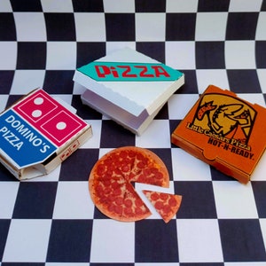 May include: Three pizza boxes on a black and white checkered surface. The boxes are for Domino's Pizza, Little Caesars Pizza, and a generic pizza box with the word "PIZZA" in red letters. A pepperoni pizza with a slice removed is also on the surface.