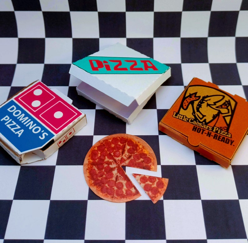 May include: Three pizza boxes on a black and white checkered surface. The boxes are for Domino's Pizza, Little Caesars Pizza, and a generic pizza box with the word "PIZZA" in red letters. A pepperoni pizza with a slice removed is also on the surface.