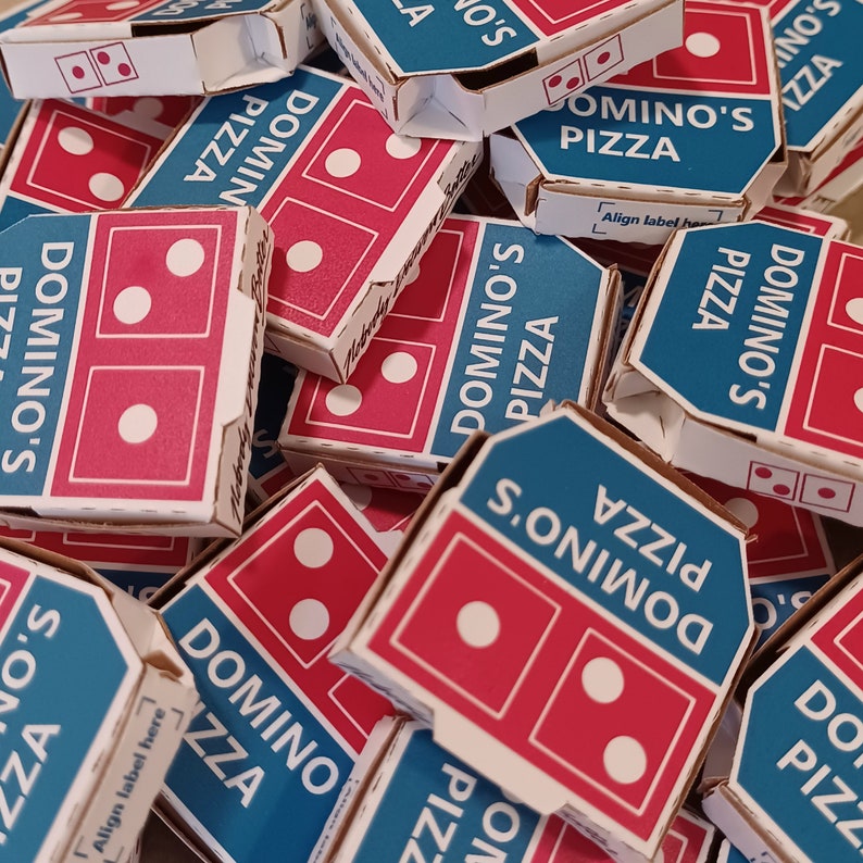 Pu&ograve; includere: Primo piano di una pila di scatole di pizza Domino's. Le scatole sono blu e rosse con il logo Domino's e le parole "Domino's Pizza" stampate su di esse. Le scatole sono impilate l'una sull'altra in un ordine casuale.