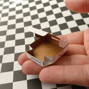 Pu&ograve; includere: Una piccola scatola per pizza in cartone bianco con un interno marrone. La scatola &egrave; aperta e il coperchio &egrave; ripiegato all'indietro. La scatola ha un'etichetta blu che dice "Align label here".