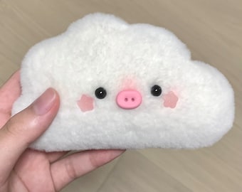 Könnte beinhalten: Ein weißes, flauschiges Plüschtier in Wolkenform mit einer rosa Schweinenase und schwarzen Augen. Das Spielzeug hat rosa Wangen.