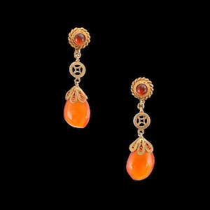 May include: A pair of gold-toned drop earrings with orange teardrop-shaped stones. Each earring features a small, round, red stone at the top, connected by a decorative chain with a circular design. The bottom of each earring has a filigree design.