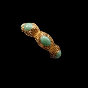 Pode incluir: Um bracelete de ouro com detalhes intrincados de filigrana e quatro pedras de jade verde ovais.